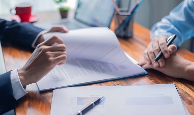 Detail of a man's hands leafing through a stack of documents while sitting at a desk