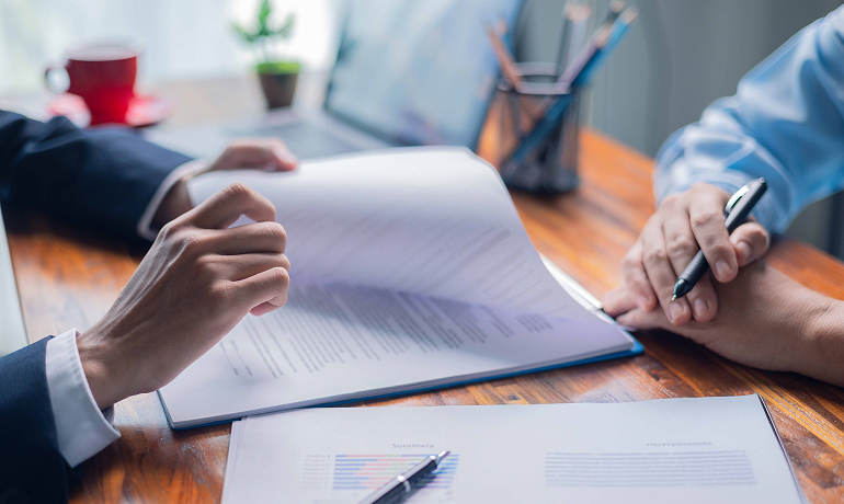 Detail of a man's hands leafing through a stack of documents while sitting at a desk