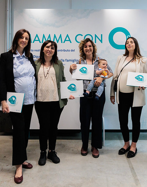 Quattro dipendenti Acea sorridono rivolte verso l'obiettivo, mentre mostrano una copia del libro illustrato "Un fiume di emozioni". La donna al centro donne tiene in braccio un neonato.