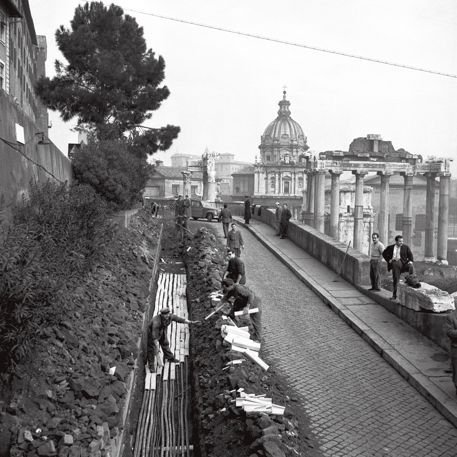 Black and white photo of workers digging the aqueduct pipes, with the Vatican in the background