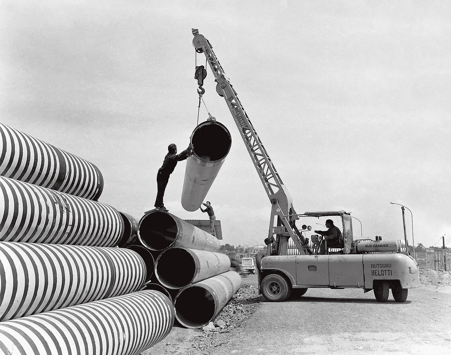 black and white photo of an old crane lifting large pipes