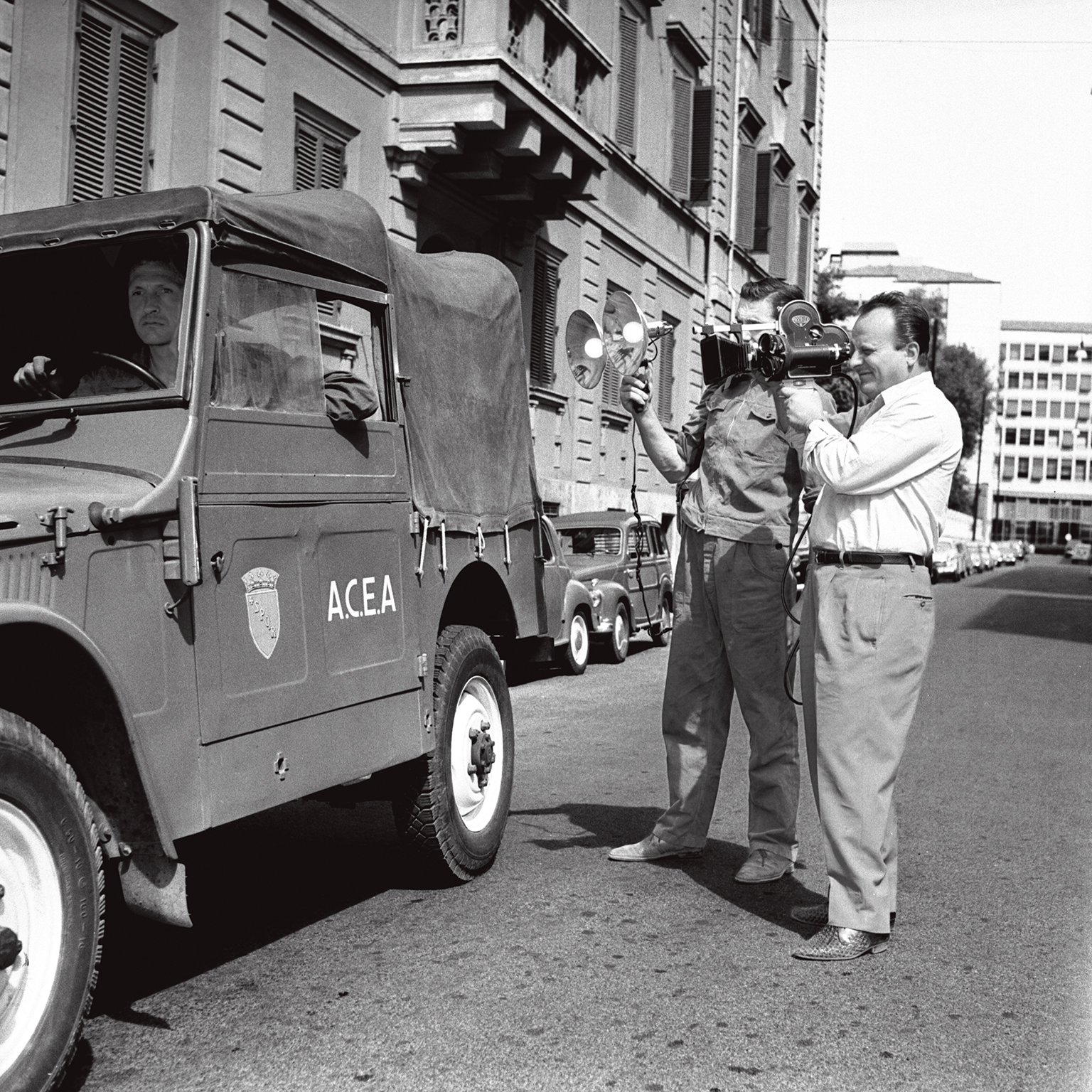 black-and-white photo of reporter recording an old acea logo van with camera
