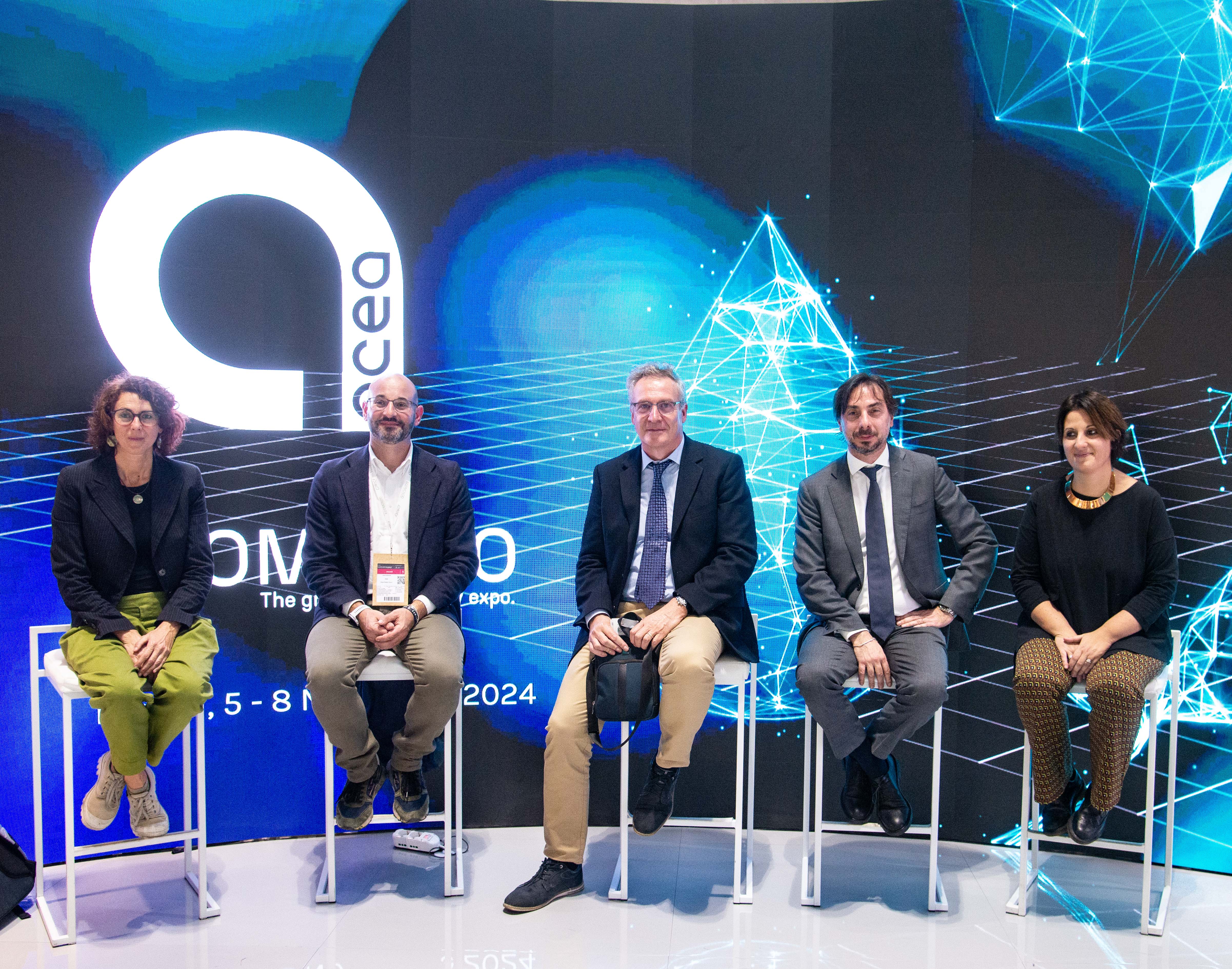 cinque speaker di una conferenza seduti su sgabelli, hanno dietro il logo acea