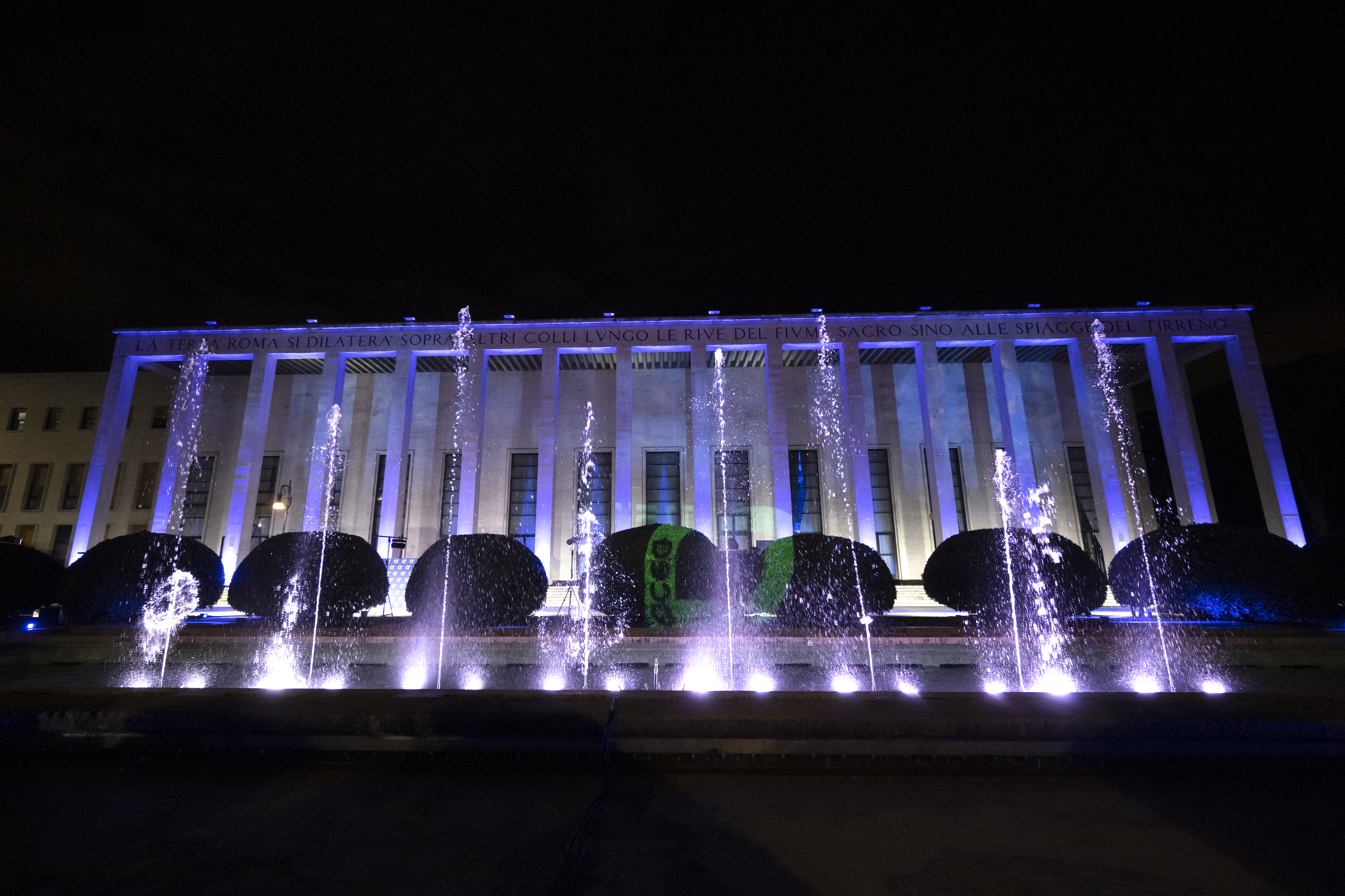 an illuminated fountain behind a building