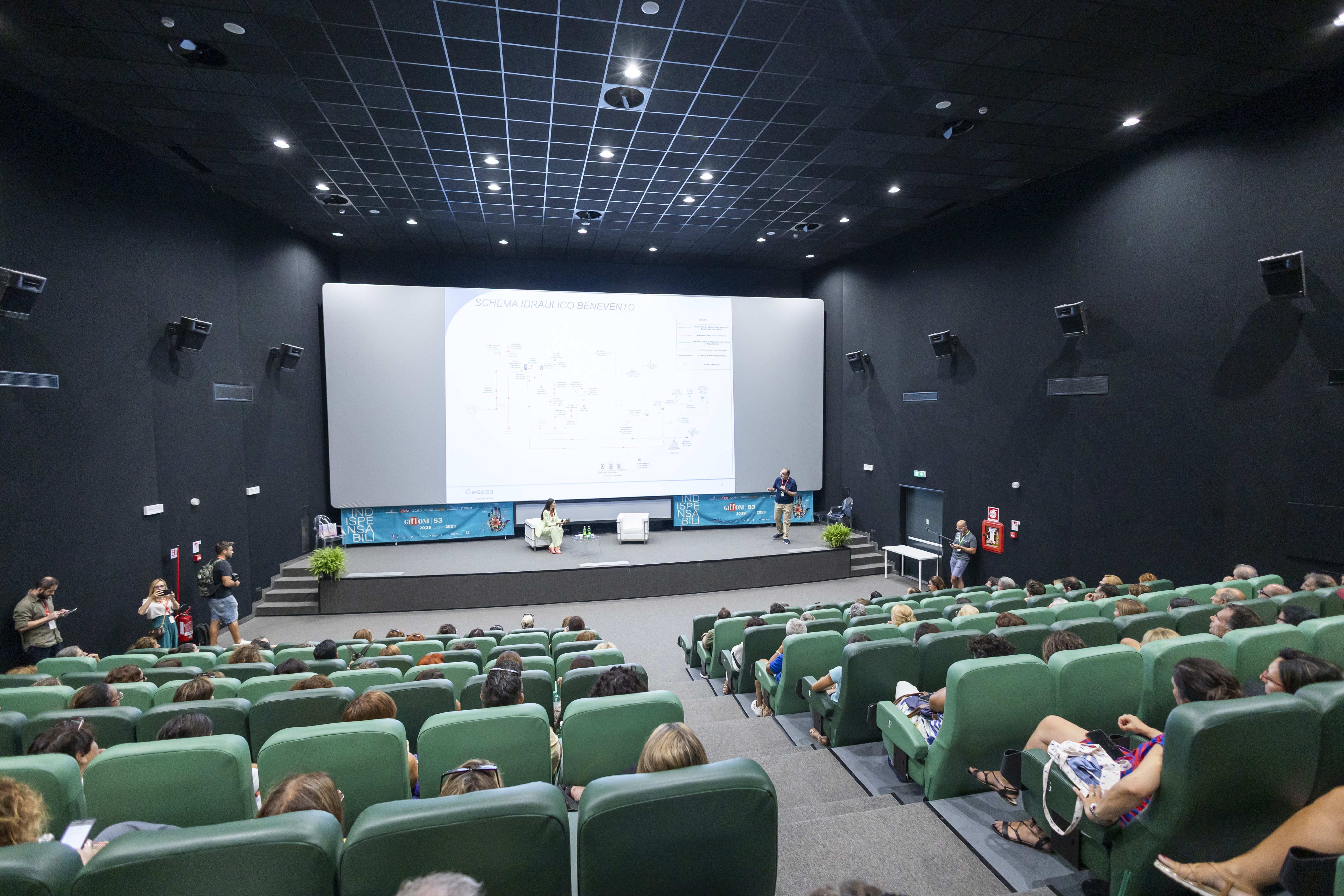 audience of people sitting in armchairs watching a speech
