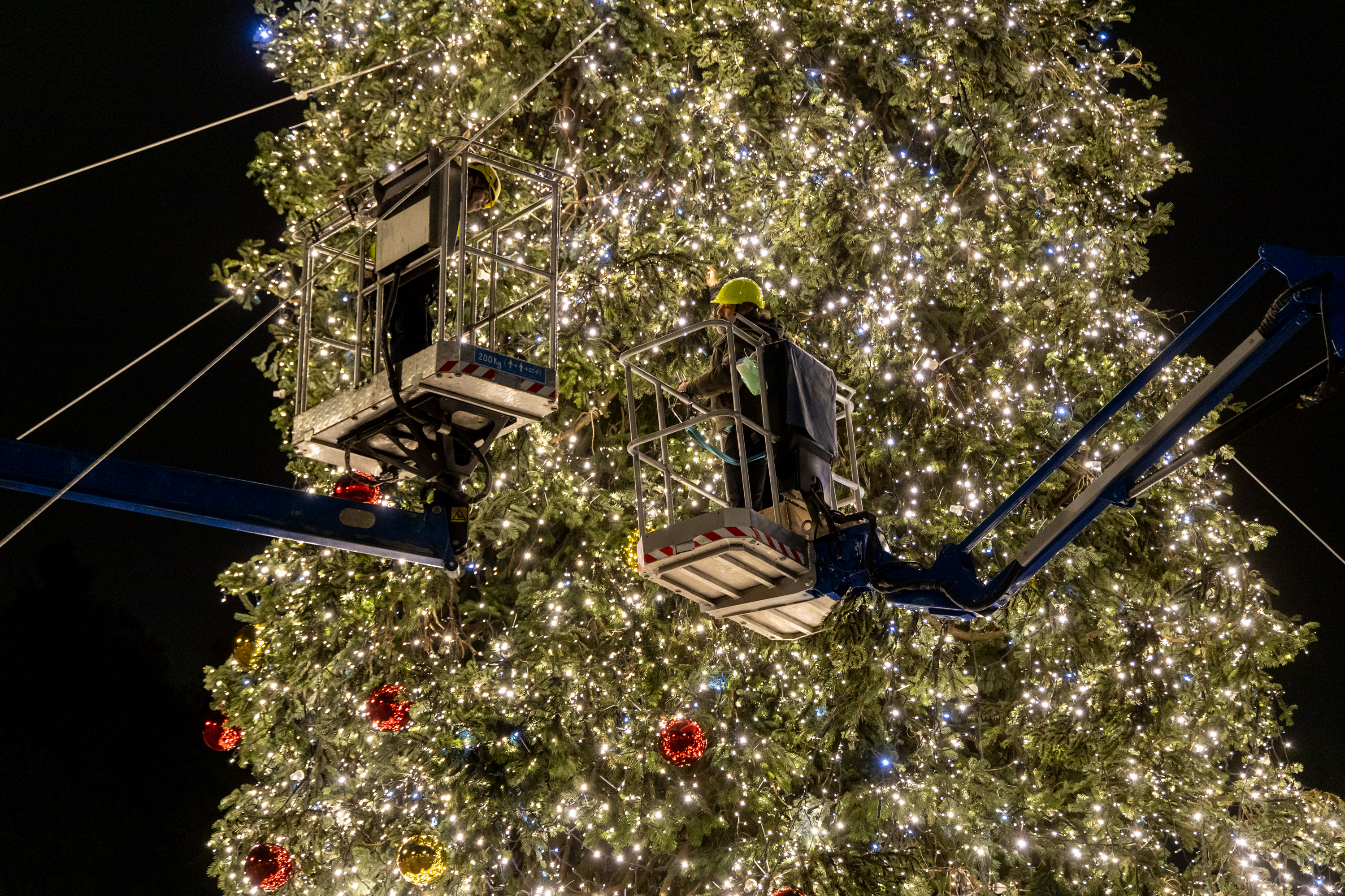 Operai su una gru che lavorano all'illuminazione dell'albero di Natale