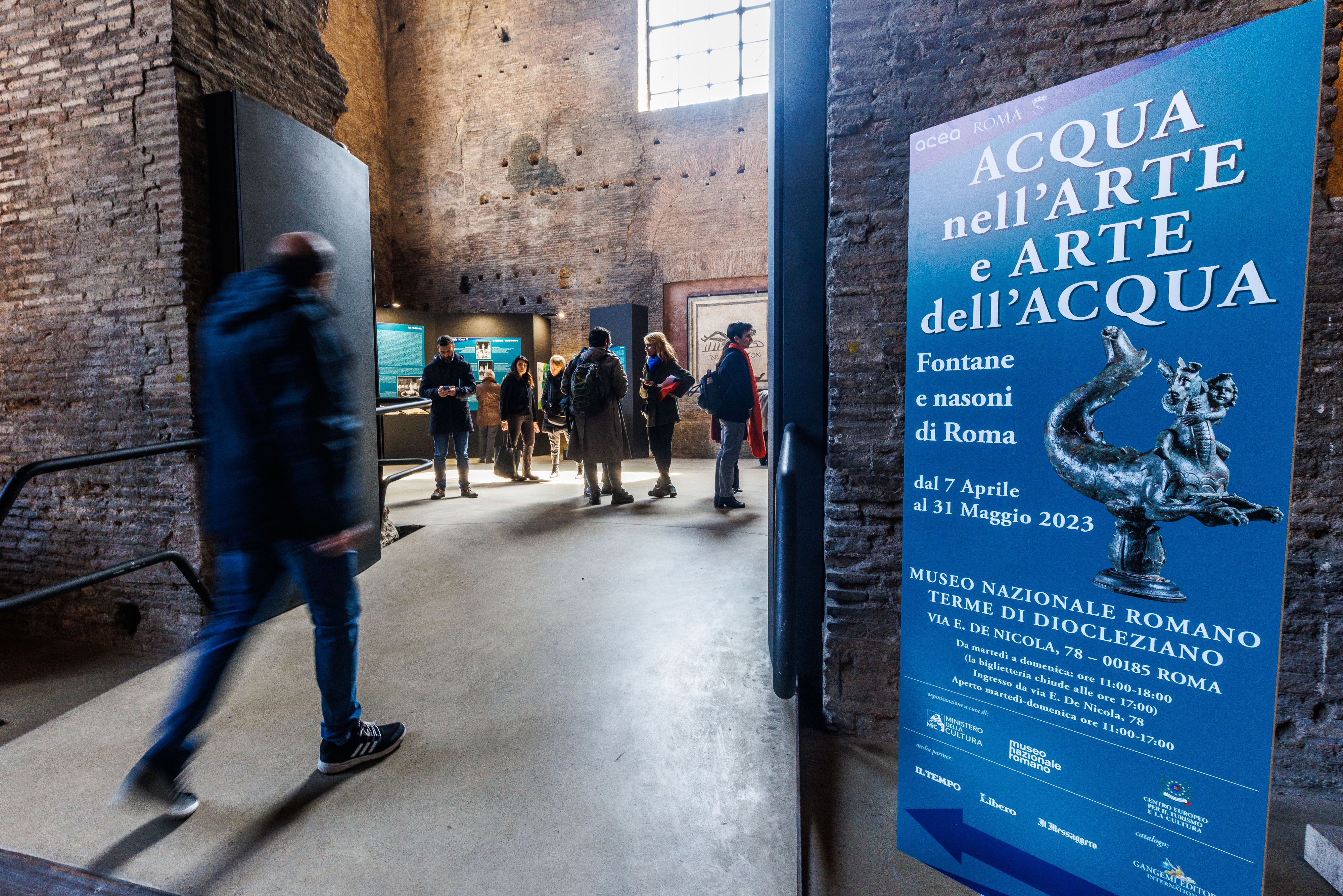 some people attending the exhibition, also a poster with the event poster can be seen