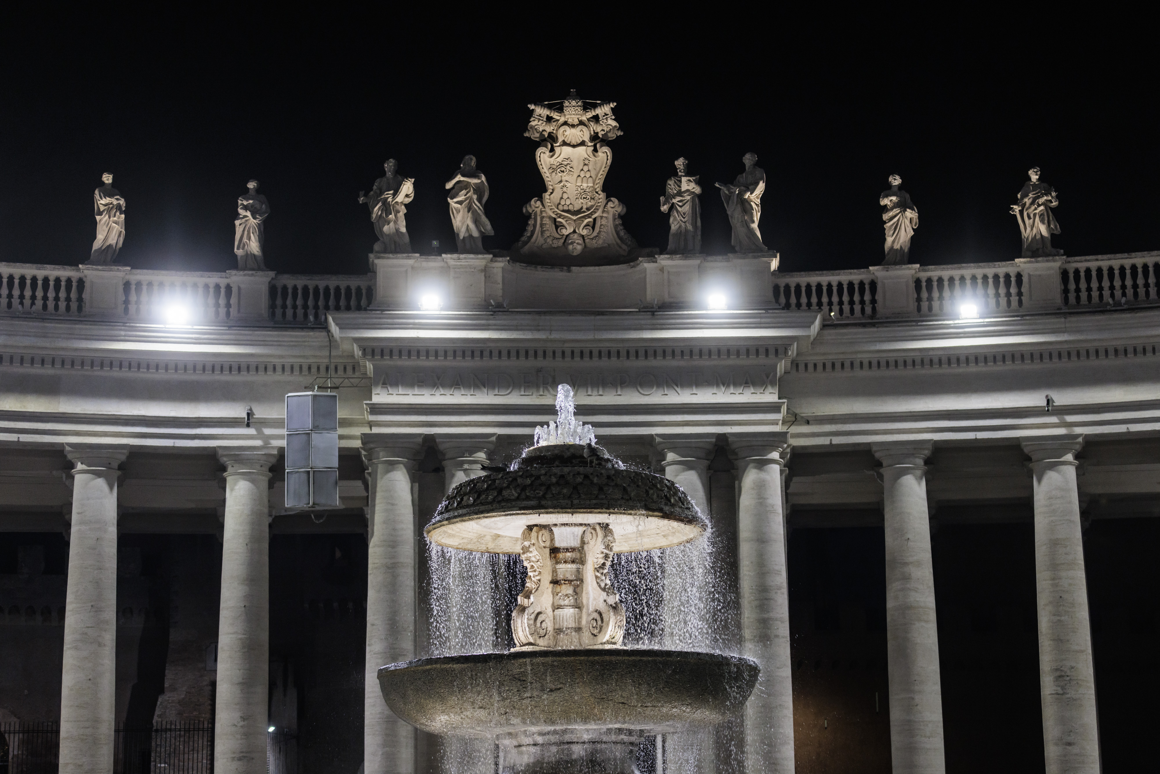 Illuminated St. Peter's Square fountain and colonnade statues